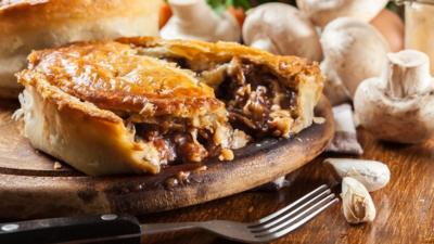 A broken meat pie with a golden crust and a juicy steak filling.